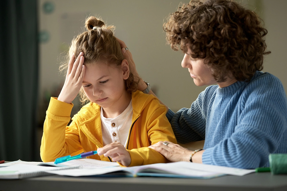 Frustrated child working on homework with parent consoling her