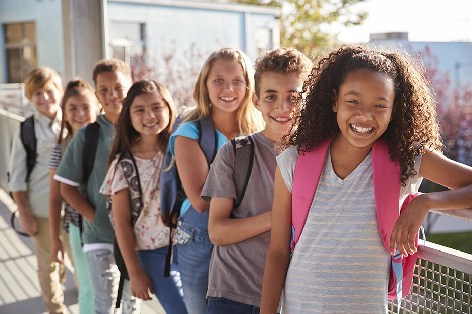 Elementary school children smiling against a railing