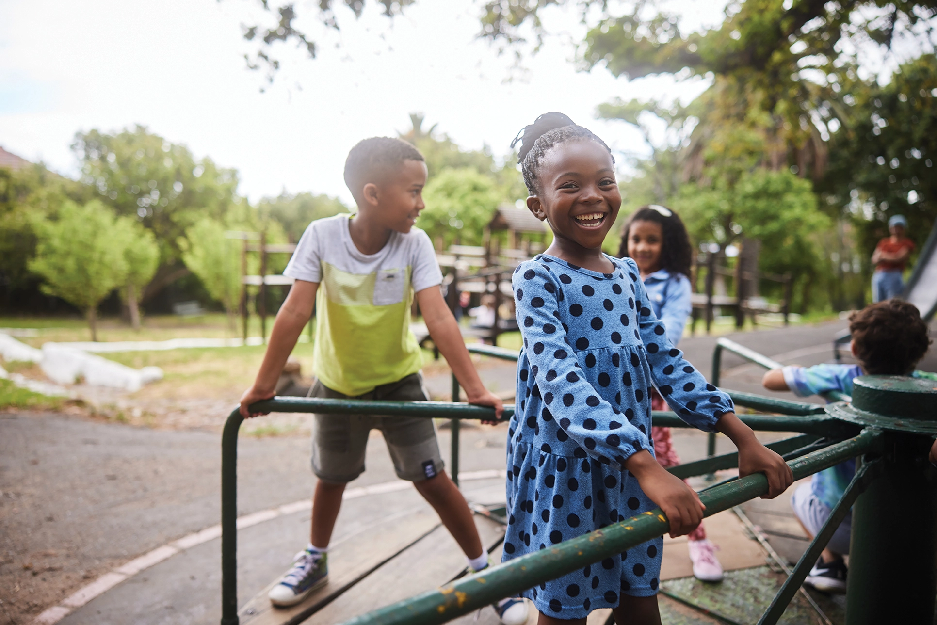 Portrait of a laughing little girl and her friends playing together on a merry-go-round in a park in summer