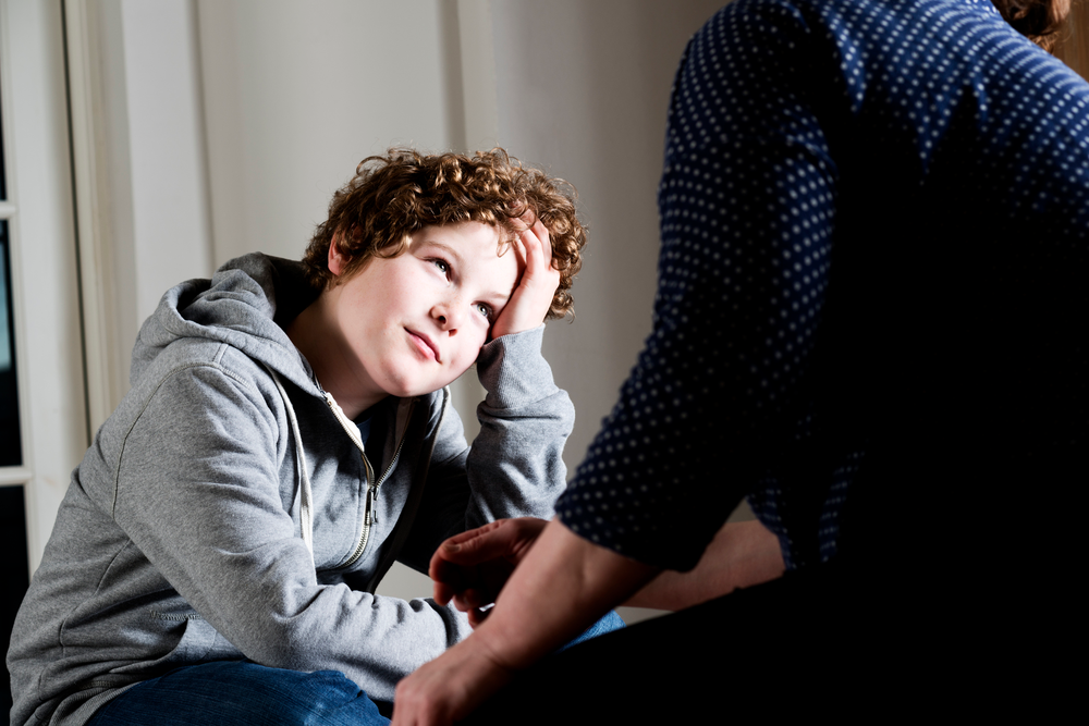 boy with hand on his forehead talking to adult