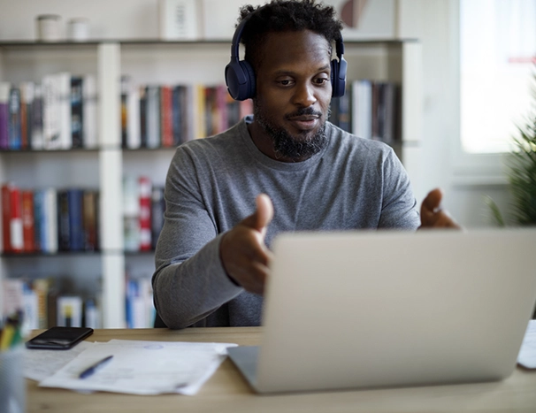 Man with bluetooth headphones having video call on laptop computer in his home office