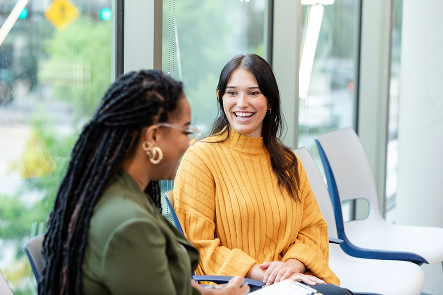 A cheerful woman smiles as she listens to a colleague discuss something during meeting.