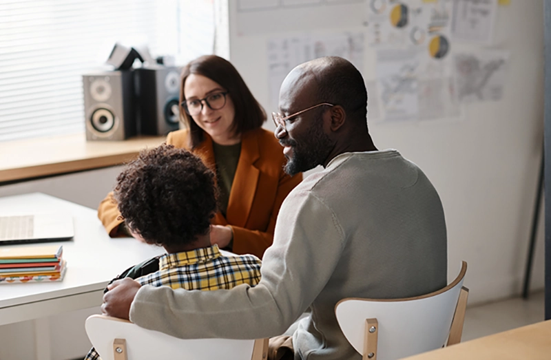 Rear view of African American father talking to teacher about school success of his son