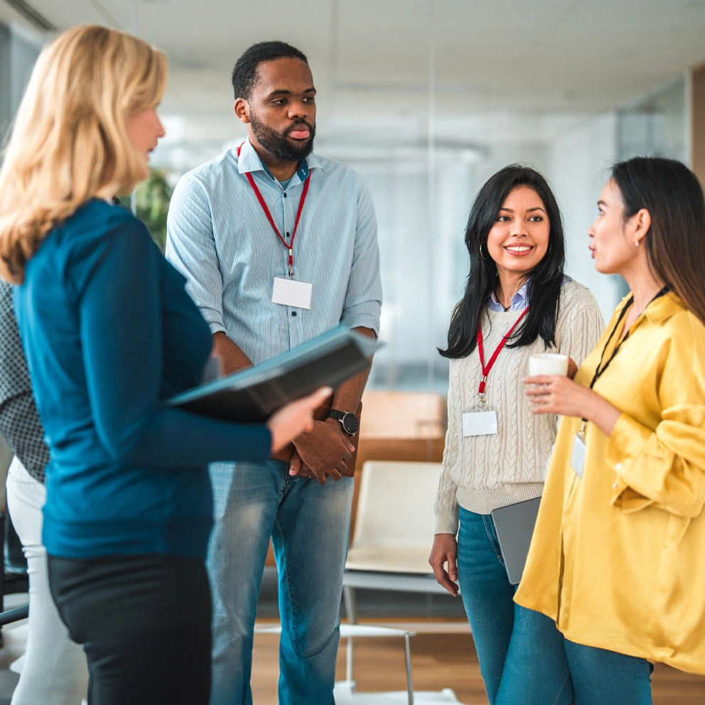 A diverse group of younger professionals wearing lanyards stands in a group, talking.