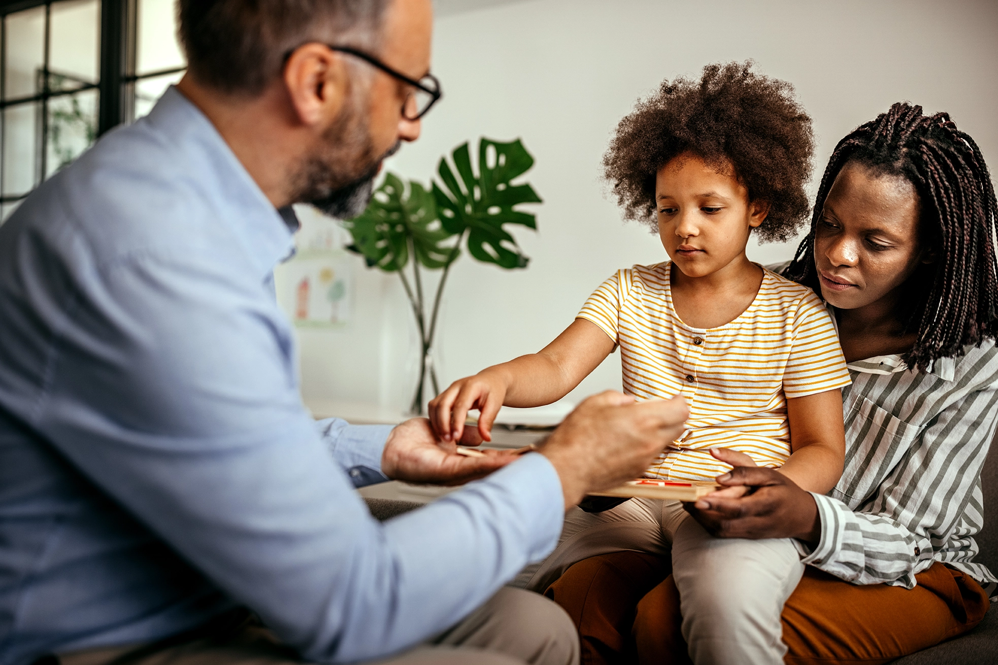 Child sitting on her mother's lap while she takes a toy from therapist's hand