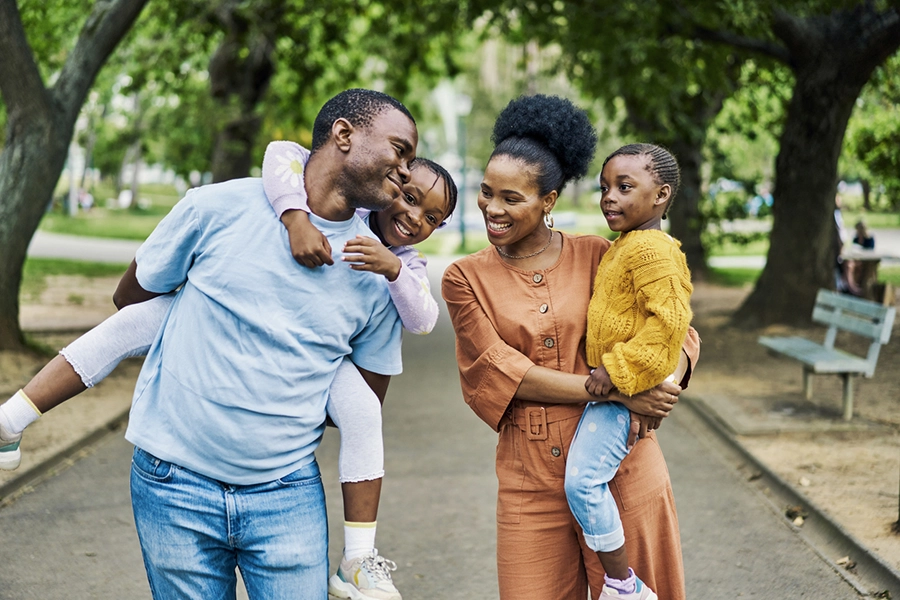 Black family, park fun and smile outdoor of a father, mother and children together with love. Summer holiday, happiness and vacation of a mother with kids walking in nature with a hug and piggy back