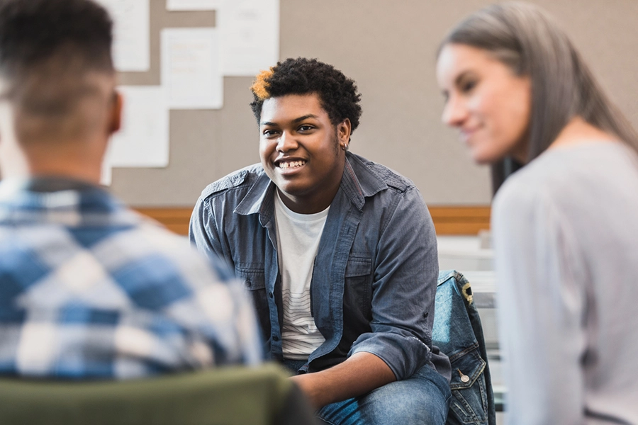 The unrecognizable female teacher is happy when the teenage boy smiles and welcomes an unrecognizable male student.