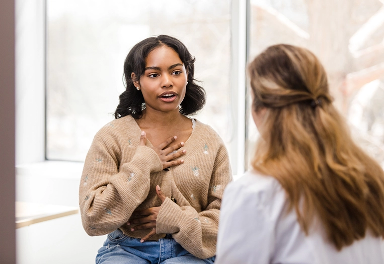 While explaining to the doctor about the discomfort in her chest, the young adult female motions her hands towards her chest.